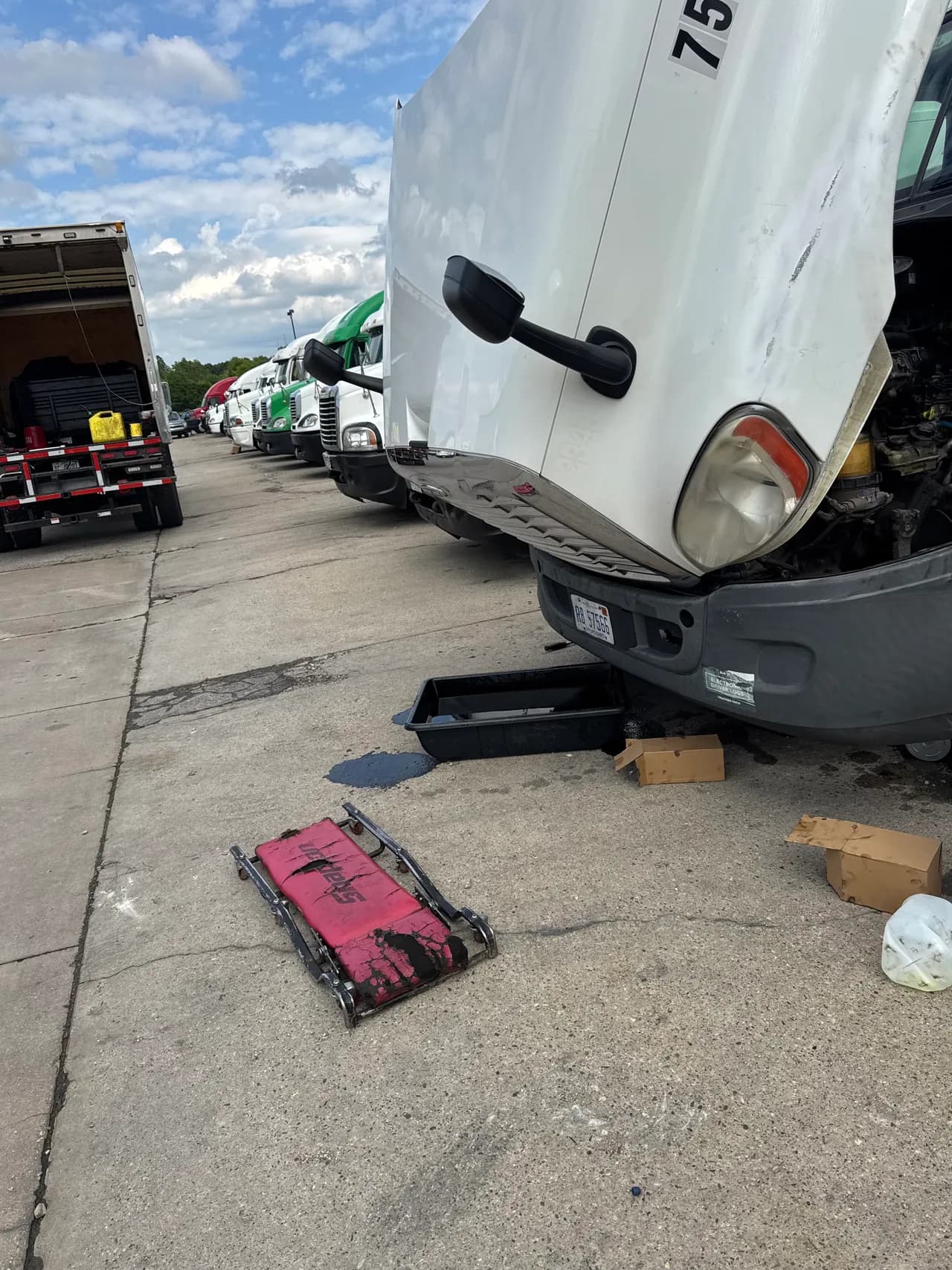 Commercial trucks lined up in a maintenance yard with a mechanic's creeper and tools