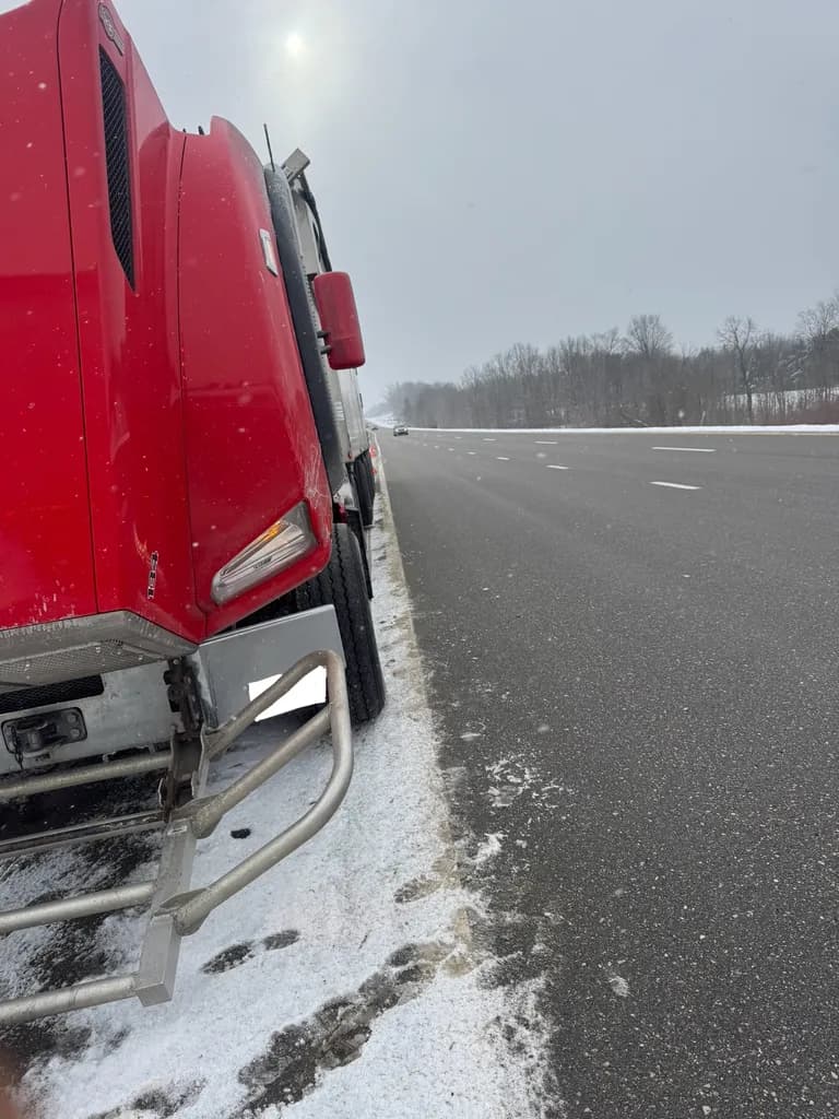 Red semi cab on a snowy highway shoulder waiting for roadside repair