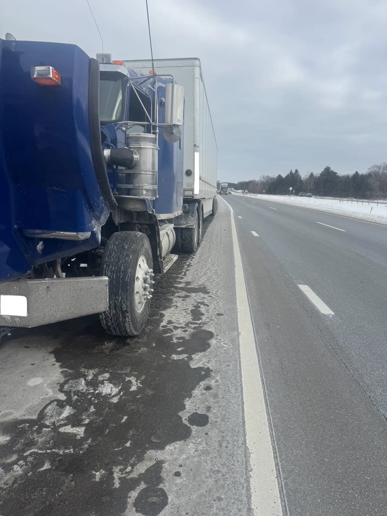 Blue semi truck stopped on a highway shoulder in winter waiting for roadside assistance