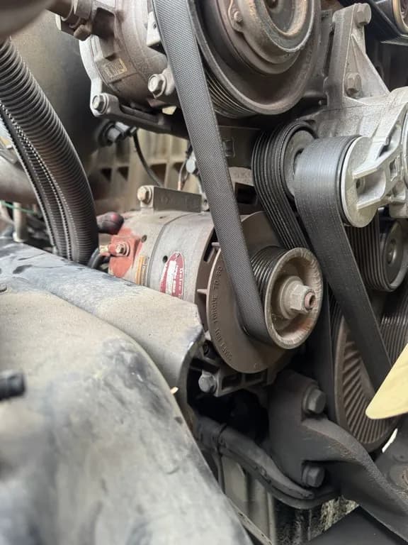 Worn serpentine belt routed around truck engine pulleys before replacement